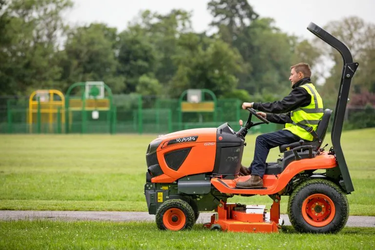 Operario conduciendo un tractor compacto sobre un campo de césped